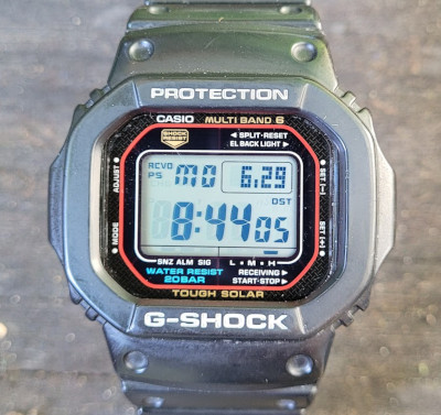 The face of my my Casio G-Shock watch as it sits on a porch railing.