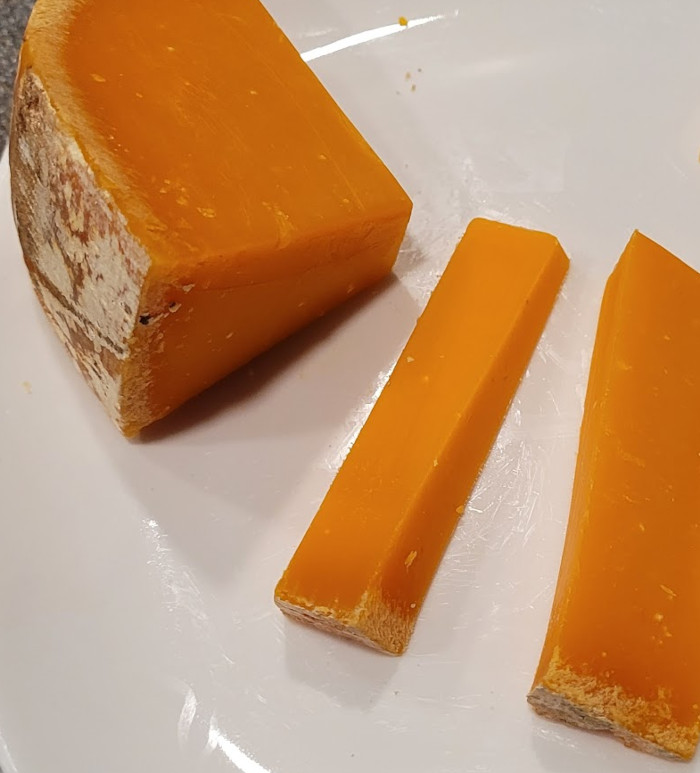 Photo of a wedge of the cheese with two slices. It’s orange with a dusty exterior.
