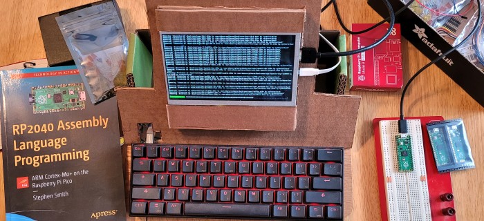 A photo of my cardboard raspberry pi computer connected to a pi pico microcontroller on a breadboard with some other parts and accessories