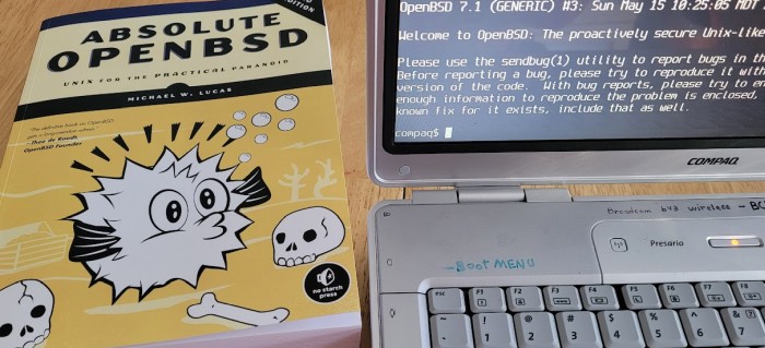 picture of the 2nd edition of the book Absolute OpenBSD next to a Compaq laptop running OpenBSD